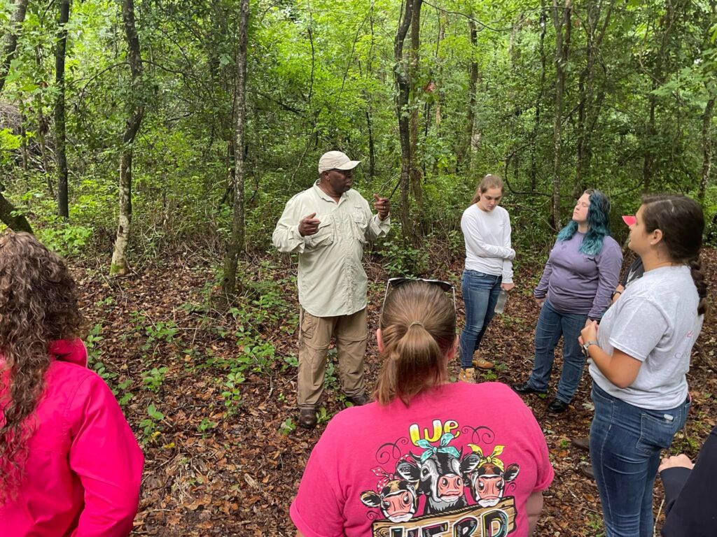 Group of people listing to a person talk surrounded by trees