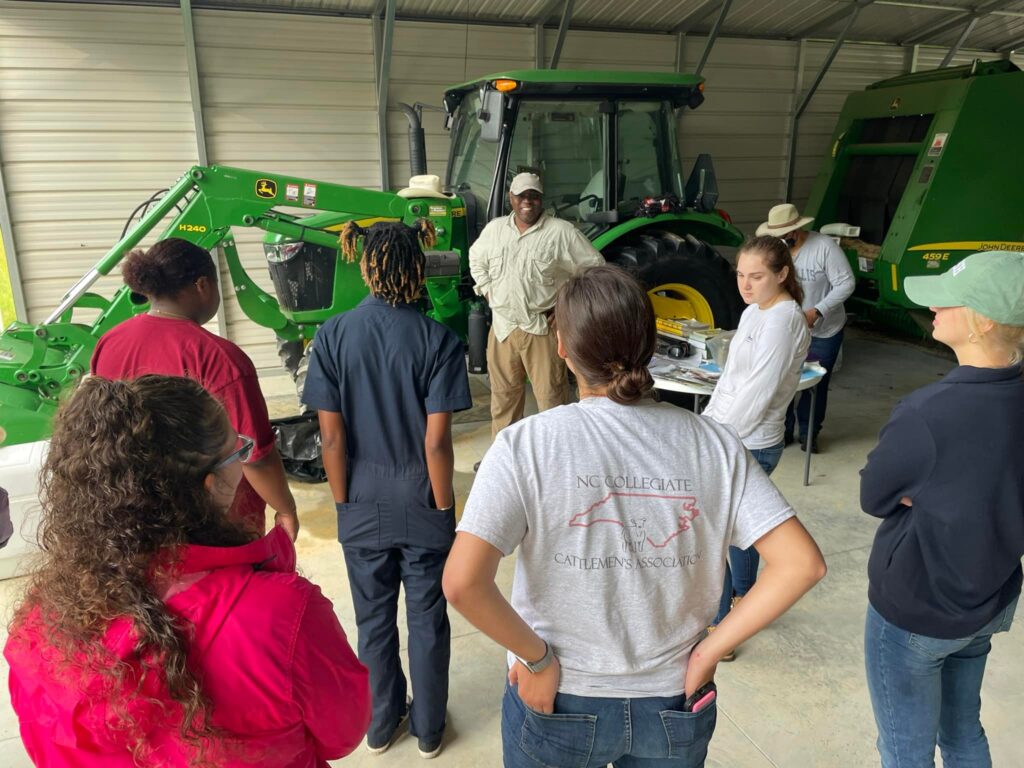 2023 Cohort standing in front of speakers in front of a John Deere tractor