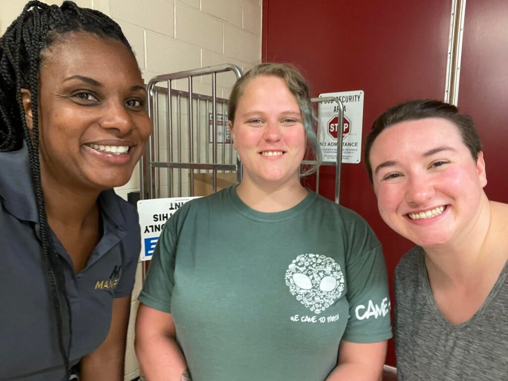 Three women smiling for camera in front of a maroon wall