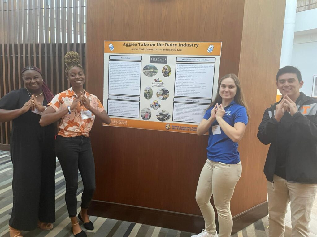 Members of 2023 Cohort posing infront of a poster of their experience