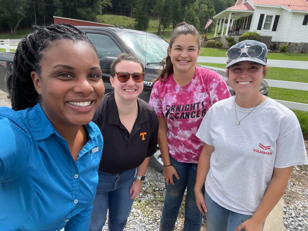 4 women smiling for the camera in front of a black truck and a house