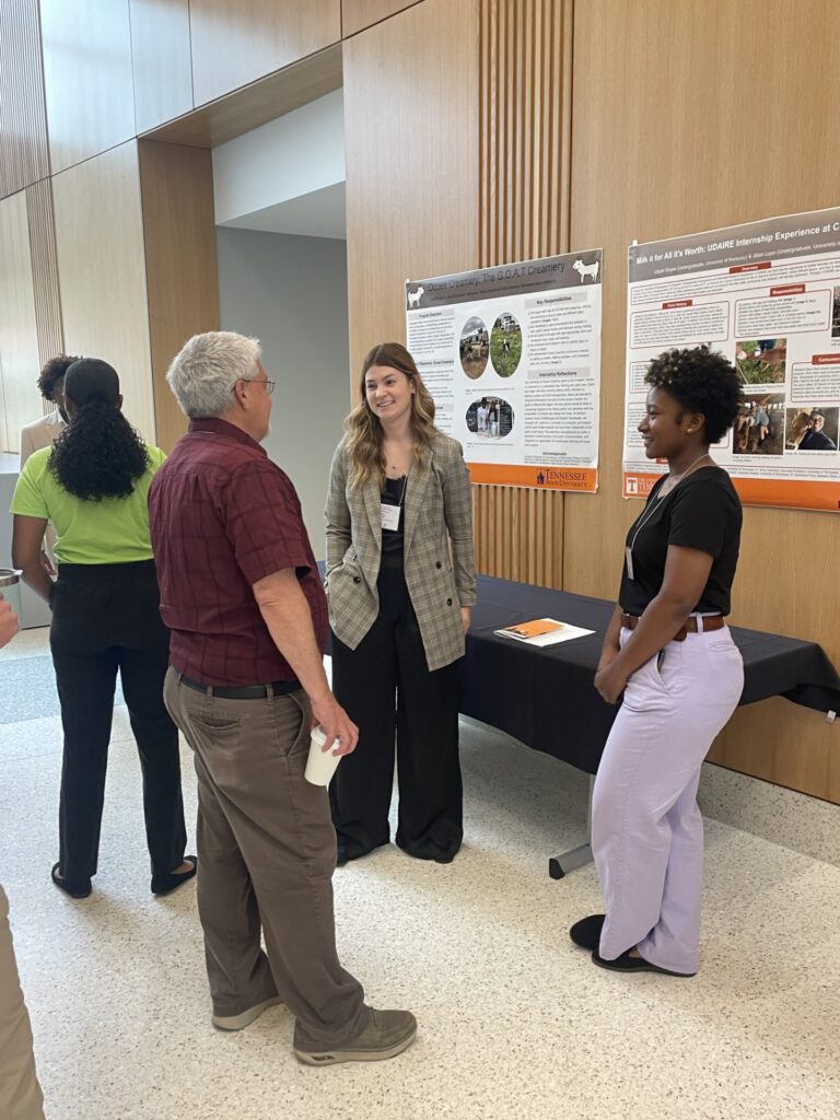 Two female students standing beside poster presentations talking with an older gentleman