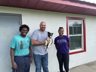 three students beside building one holding a dog