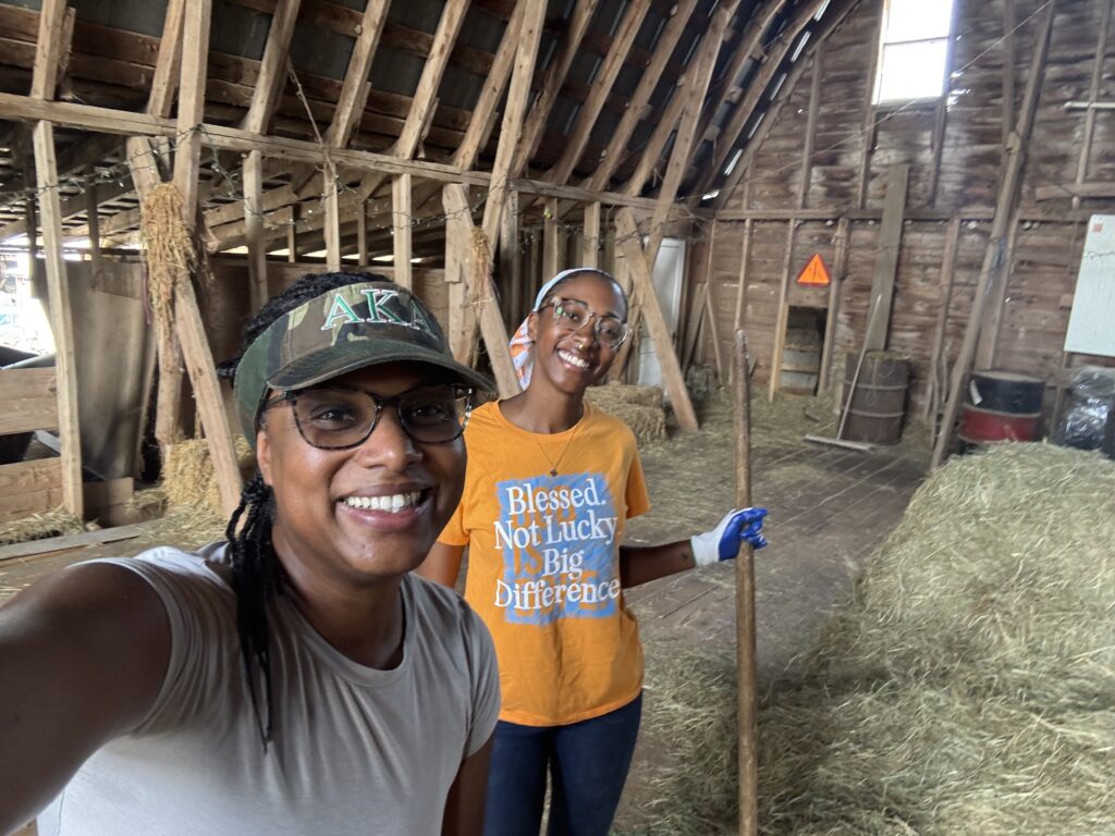 Two people smile for the camera with bales of hay next to them