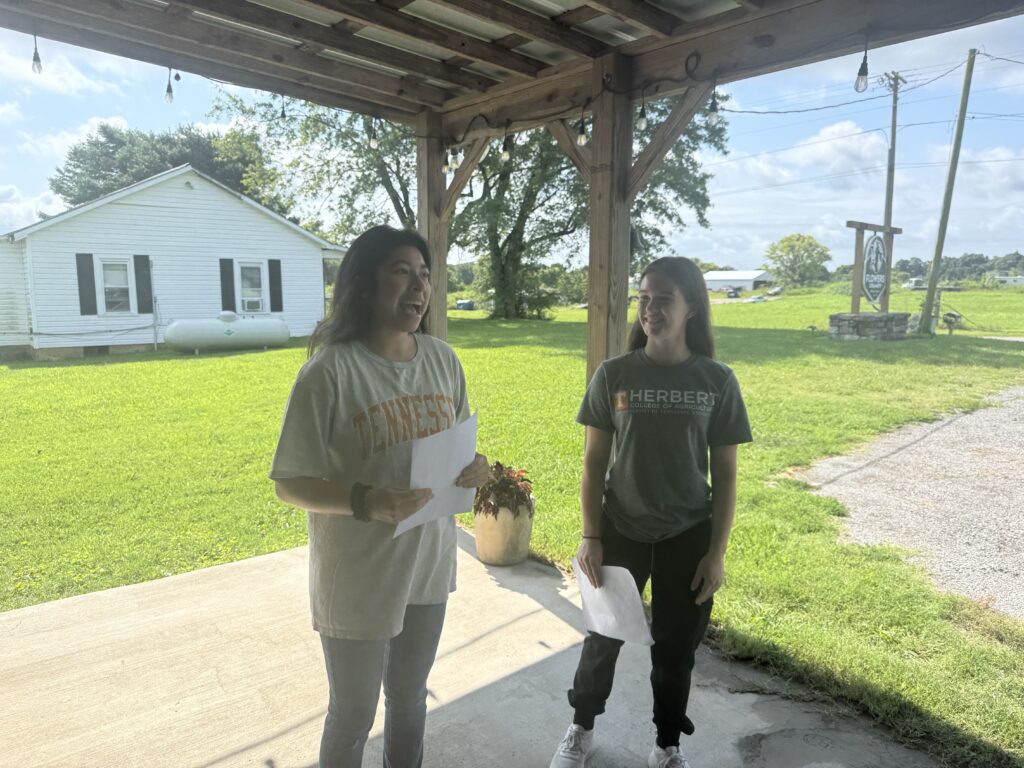 One person looks on as another person is speaking, holding papers