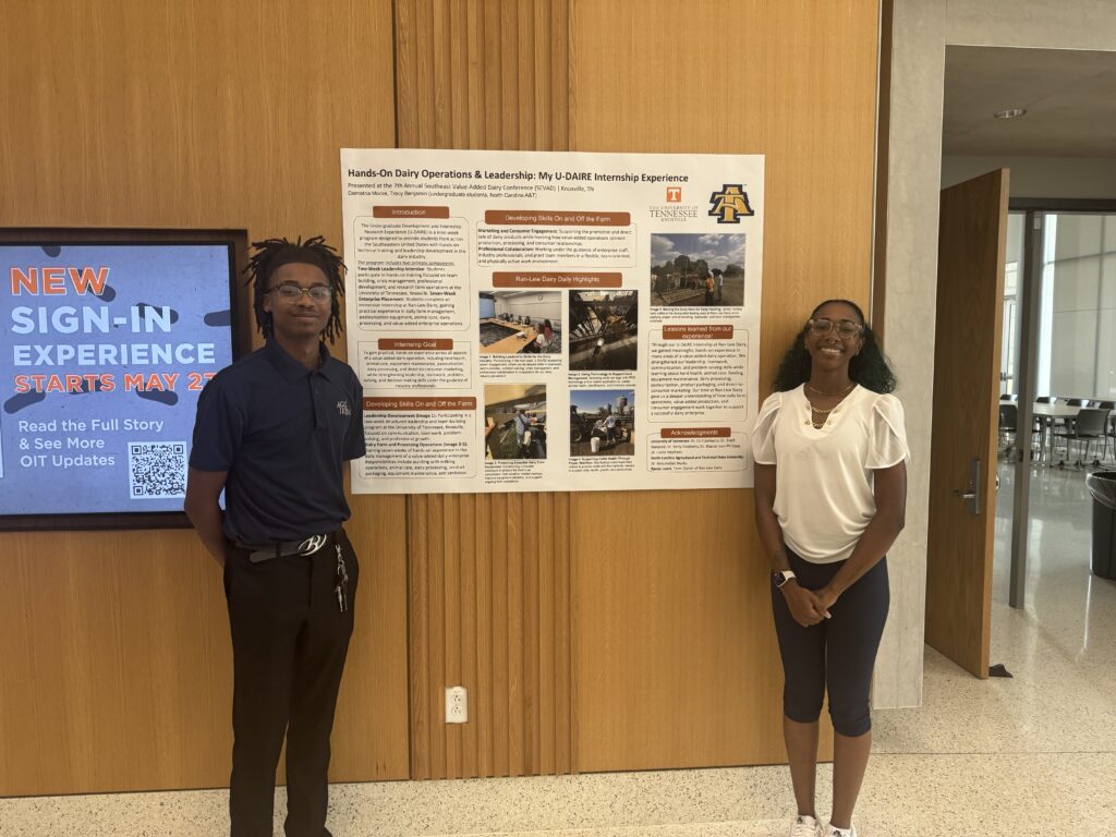 A male and female student stands next to their poster